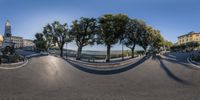 a fish eye lens photo of a street scene in italy with trees on either side and an orange building in the distance