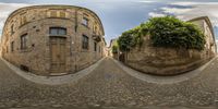 a 360 - eye shot of an old city street shows buildings with trees in front and a bench on the side of each of them