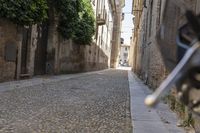 an alleyway with stone floors, buildings and a bike parked on the sidewalk with trees around it