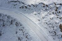 two people are cross country skiing on a snowy slope with rocks behind them a black car is driving across the snow