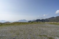 a field with rocks and grass with mountains in the distance under a partly cloudy blue sky