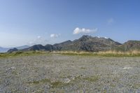 a field with rocks and grass with mountains in the distance under a partly cloudy blue sky