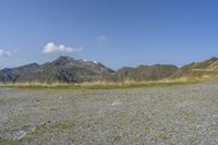 a field with rocks and grass with mountains in the distance under a partly cloudy blue sky