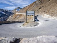 sign on a road in front of some mountains and snow covered hills on the side of the road