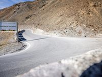 sign on a road in front of some mountains and snow covered hills on the side of the road