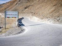 sign on a road in front of some mountains and snow covered hills on the side of the road