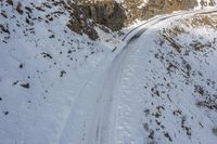 a view from a mountain looking down onto the track through the snow and rocks that leads to the road