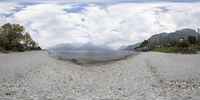 a fish - eye view photo of a beach with gravel in the foreground and mountains in the background