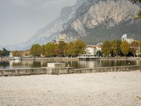 a park bench is on the shore next to water and rocks and a mountain range