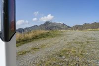 a field of grass in the middle of mountains with rocks and grasses on the ground