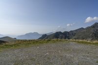 a mountain range with a rocky terrain covered with grass and plants near by, under a blue sky