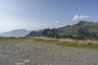 a mountain range with a rocky terrain covered with grass and plants near by, under a blue sky