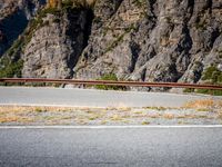 a person riding their bicycle down the street next to a mountain cliff side road and a bike path