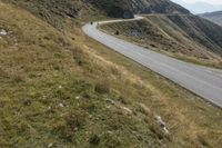 a long winding road cuts through the mountains, with a cyclist on it, riding down a curve