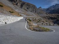 a curved road stretches off of the side of a mountain, with a stone wall in the foreground