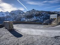 a long curving mountain road is shown on a sunny day with snow capped mountains and a traffic signal