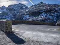 a long curving mountain road is shown on a sunny day with snow capped mountains and a traffic signal