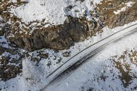 a aerial view of a train on the tracks near snow - covered mountains and rocks