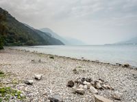 rocky shore with trees along side, and mountains in the background over looking water and hills