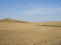 a rural landscape with dirt, grass and a single bench facing the left, in front of an open sky