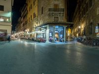 a couple of buildings in the middle of a town at night, and people sitting at tables near the street