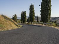 an empty street on a sunny day in the countryside with tall trees and hills to the side