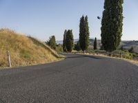 an empty street on a sunny day in the countryside with tall trees and hills to the side