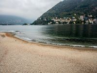 an empty beach on the shore of a mountain lake, with houses and seagulls in the background