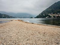 an empty beach on the shore of a mountain lake, with houses and seagulls in the background