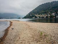 an empty beach on the shore of a mountain lake, with houses and seagulls in the background