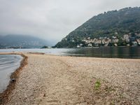 an empty beach on the shore of a mountain lake, with houses and seagulls in the background