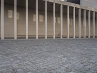 a brick courtyard that has several pillars and columns around it and several people walking and sitting on the ground