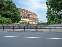 a view of a stadium from the street, showing many trees and bushes in the distance