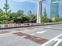 two arrows pointing in opposite directions on a road that passes under a street sign with two smaller buildings in the background