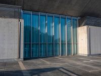 a sidewalk that has several glass doors next to it with buildings in the background behind