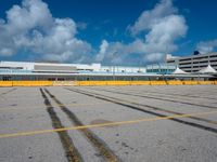 an empty parking lot filled with lots of buildings and trucks in the background of a cloudy blue sky