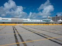 an empty parking lot filled with lots of buildings and trucks in the background of a cloudy blue sky