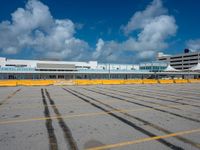 an empty parking lot filled with lots of buildings and trucks in the background of a cloudy blue sky