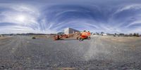 a pair of orange work lift trucks on a concrete road next to a building under a cloudy sky