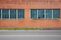 an empty street next to a large red brick building with several glass windows on it