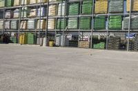 a fenced in area is next to many stacks of crates and trucks and a blue sky