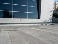 an image of skateboarder performing trick on concrete and glass wall outside building at daytime