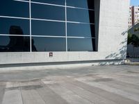 an image of skateboarder performing trick on concrete and glass wall outside building at daytime