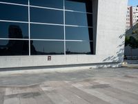 an image of skateboarder performing trick on concrete and glass wall outside building at daytime