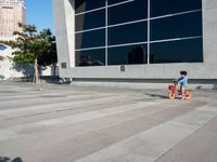 a little kid riding his bicycle on the sidewalk next to a building with a glass window