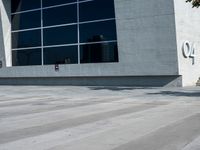 the man is walking down the side walk with his skateboard on his foot in front of a large building