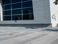 the man is walking down the side walk with his skateboard on his foot in front of a large building