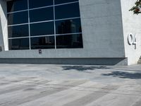 the man is walking down the side walk with his skateboard on his foot in front of a large building