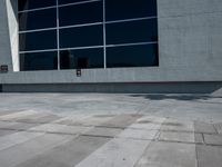 the man is walking down the side walk with his skateboard on his foot in front of a large building