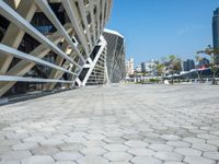 a cobble stone walk way in front of a modern, concrete building with a blue sky